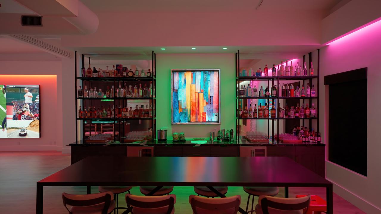 Private bar with colorful lighting, bottle displays, and multiple integrated digital art and media walls